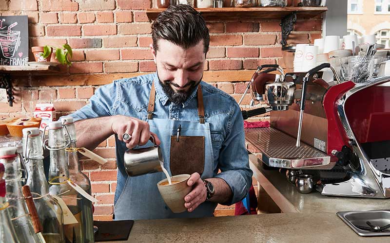 barista pouring milk into cup of coffee