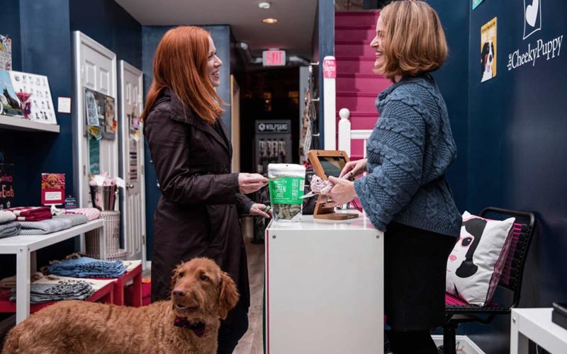 woman with her dog in front of a retail sales counter talking to retail salesperson standing behind the counter