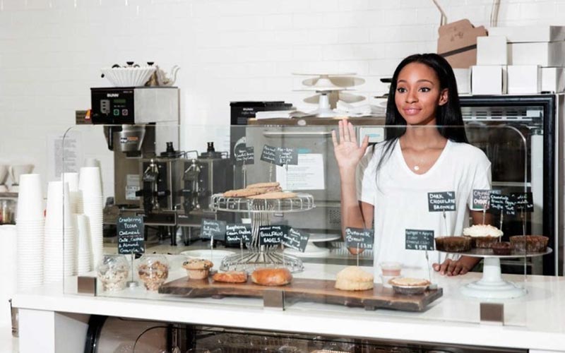 woman behind the counter at a bakery waving her hand to say hello