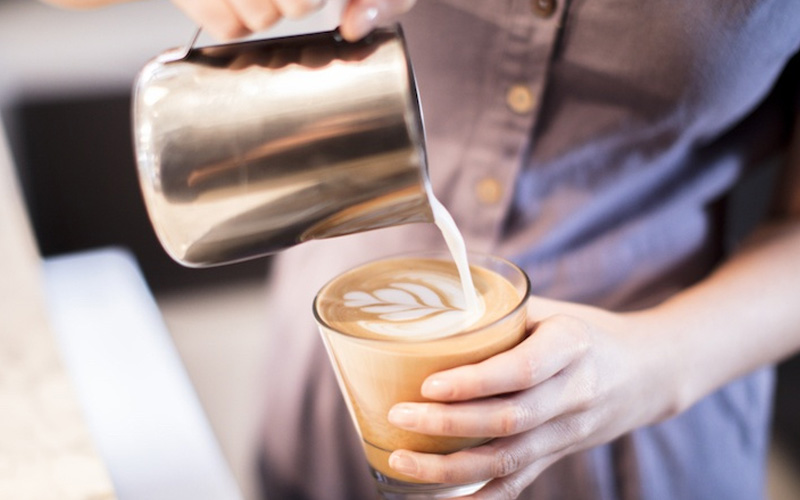 barista pouring milk to make latte art in a cup of coffee