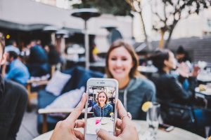 Photo of an iPhone screen showing a woman being photographed at a table at an outdoor area of a restaurant