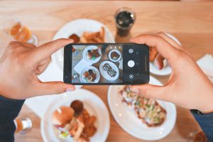 Overhead shot of someone taking a photo with their iPhone of a table with four plates of food on it