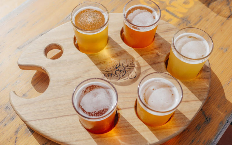 A flight of three beers on a wooden board with the name Wood and Stone printed on it.