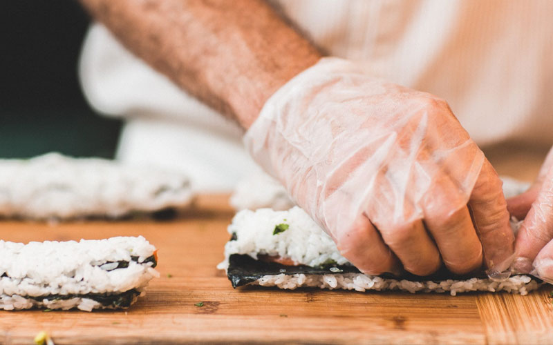 Primer plano de un chef enrollando un rollo de sushi y usando guantes de plástico.