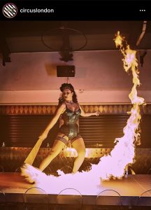 A photo from Circus' Instagram of a female circus performer swinging a fire-lit torch.