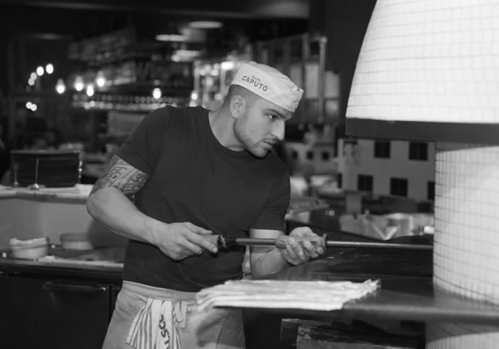 black and white photo of chef sliding pizza into pizza over